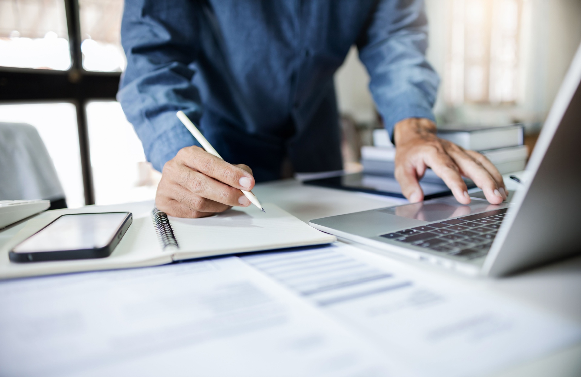 Regnskapsfører ser på en laptop mens han skal notere med penn i en notatbok